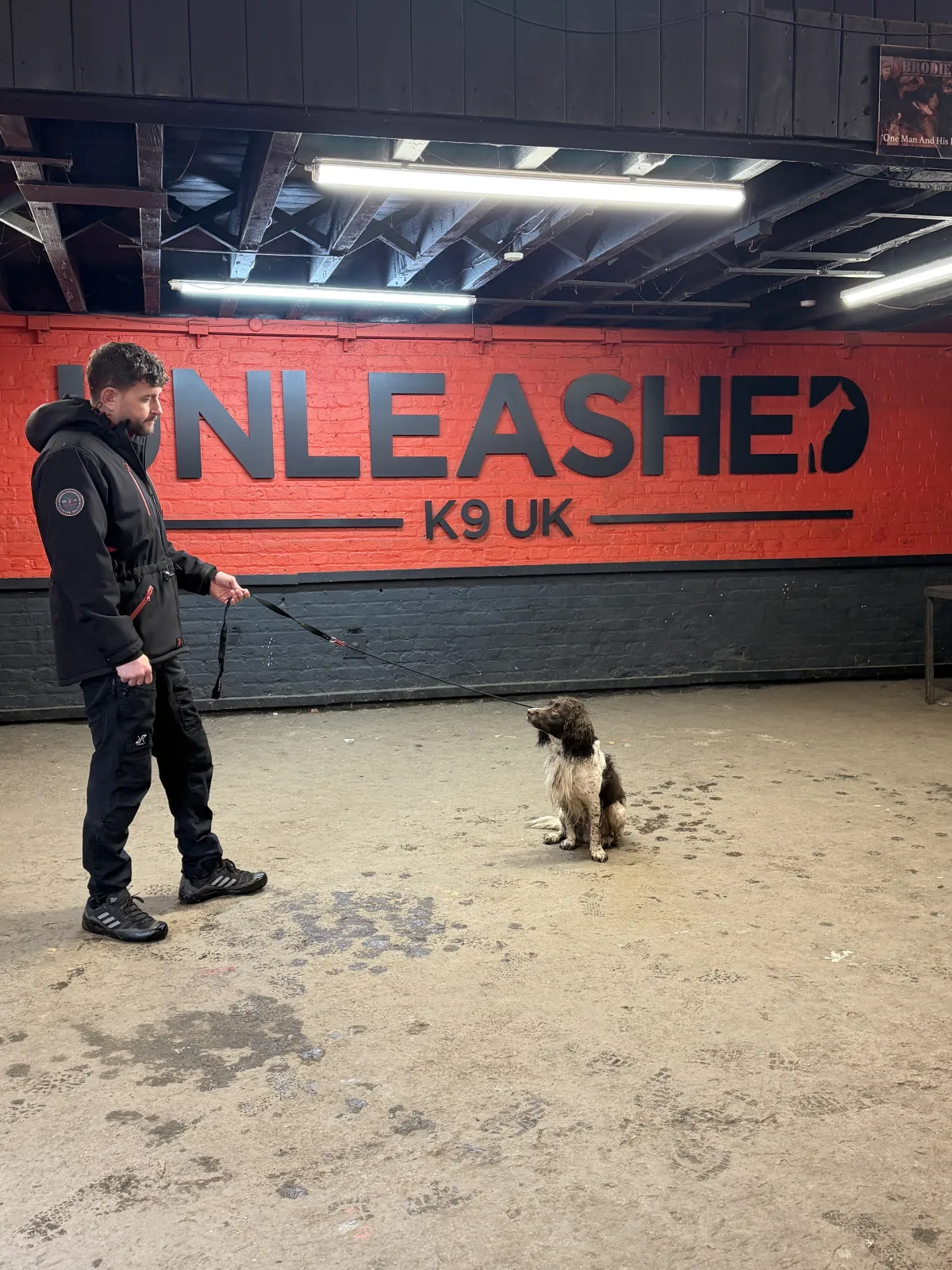 Danny with dog at sit command in front of Unleashed K9 sign
